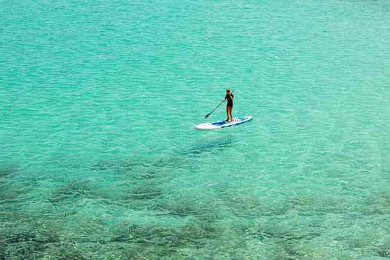 Person der padler stående på et paddleboard i klart turkisblåt vand. (AI-genereret tekst)