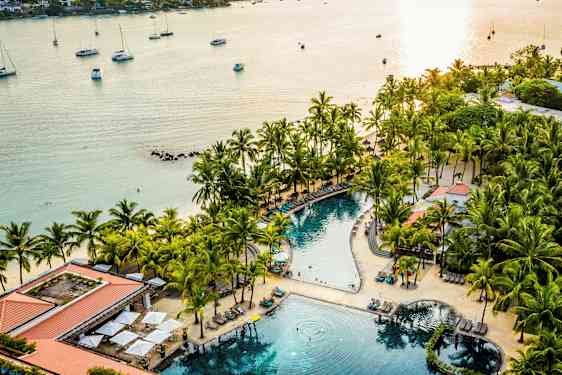 Et strandresort med en pool omgivet af palmer og liggestole nær havet. (AI-genereret tekst)