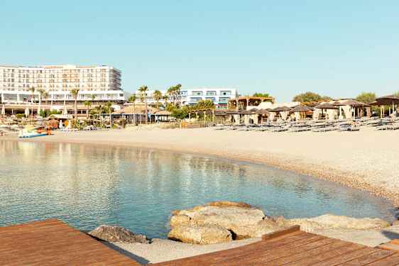 Strand med liggestole og parasoller, hotelbygninger i baggrunden. (AI-genereret tekst)