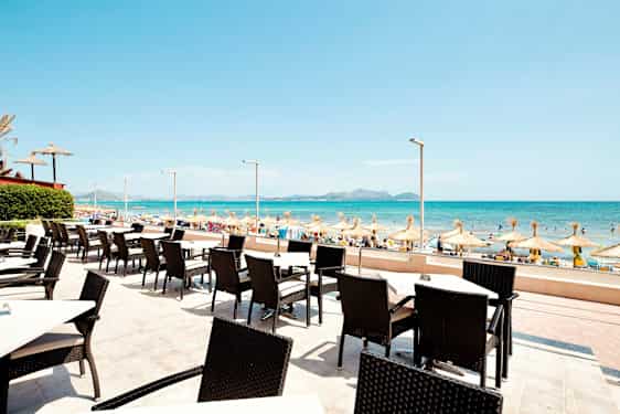 Udendørs servering med udsigt til en sandstrand og havet med parasoller. (AI-genereret tekst)