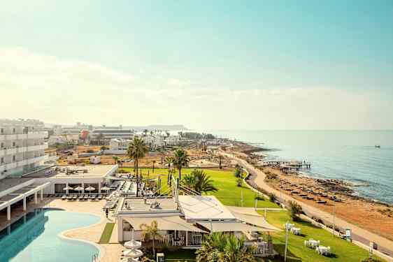 Billede der viser et hotelområde med pool og grønne områder tæt på havet. (AI-genereret tekst)