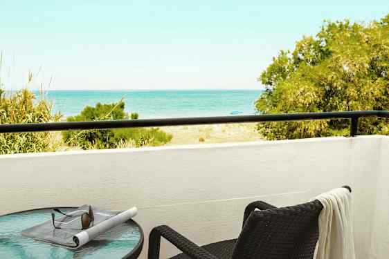 En altan med udsigt til havet, et bord med solbriller og en avis samt en stol med et håndklæde. (AI-genereret tekst)