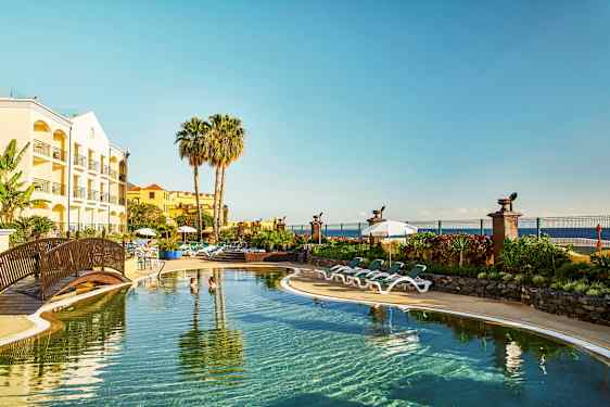 Hotel med pool, liggestole og palmetræer ved kysten. (AI-genereret tekst)