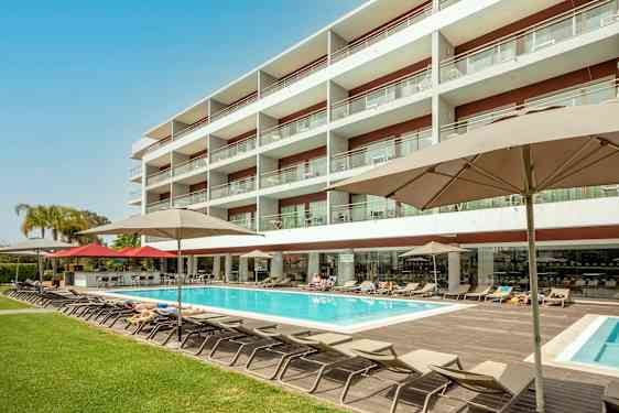 Hotelbygning med pool og liggestole. (AI-genereret tekst)