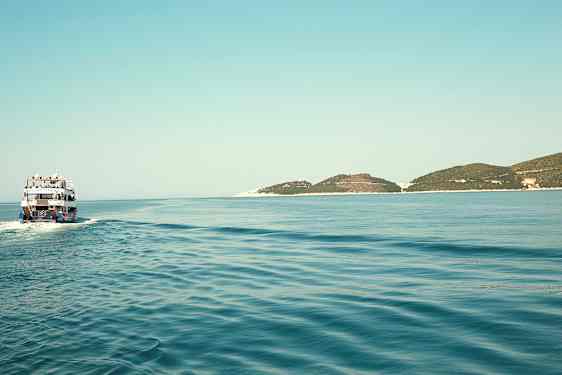 En båd sejler over et stille hav med nogle lave øer i horisonten. (AI-genereret tekst)