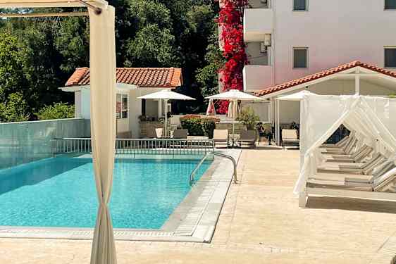 En udendørs swimmingpool med liggestole og et hvidkalket hus i baggrunden. (AI-genereret tekst)