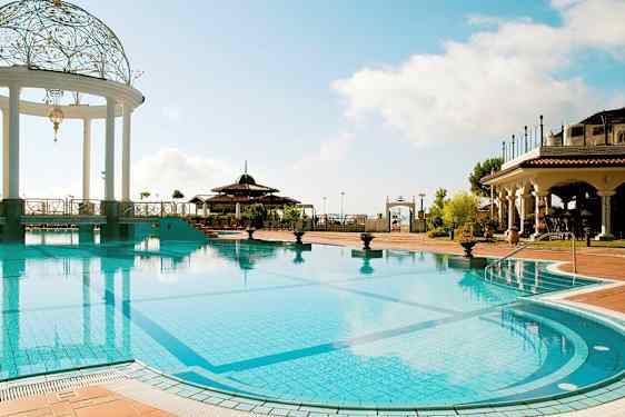 En udendørs swimmingpool med en dekoreret pavillon og omgivet af bygninger i middelhavsstil. (AI-genereret tekst)