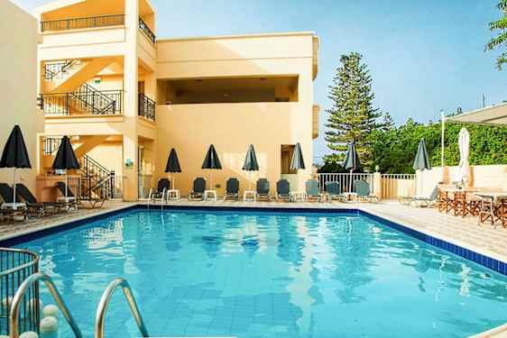 Udendørs pool med liggestole og parasoller, omgivet af bygninger og grønne områder. (AI-genereret tekst)