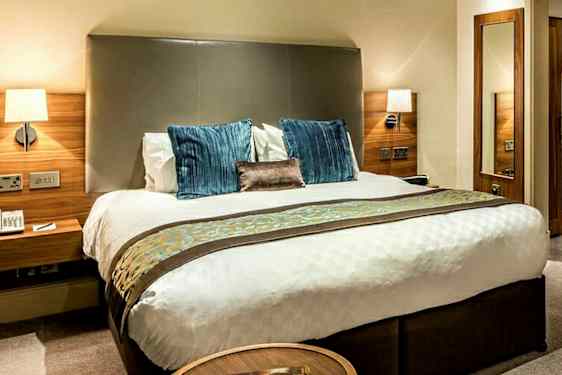 Billede af et hotelværelse med en dobbeltseng, sengebord og garderobe i træ. (AI-genereret tekst)