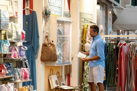 En butik ved en gade, der sælger tøj og tilbehør, med tasker og kjoler synlige i udstillingsvinduet. (AI-genereret tekst)