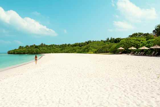En kvinde går på en sandstrand med turkis vand og grøn vegetation i baggrunden. (AI-genereret tekst)
