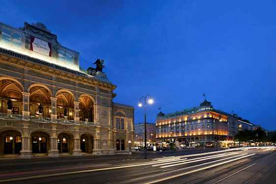 Et aftenbillede med en oplyst historisk bygning til venstre og en gade med lysstriber fra forbipasserende køretøjer. (AI-genereret tekst)