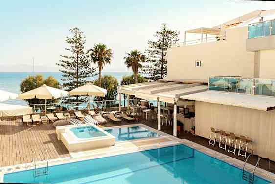 Et hotelområde med en pool, solsenge og parasoller ved havet. (AI-genereret tekst)