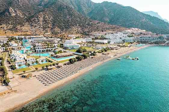 Luftfoto af en kystlinje med hotelkompleks ved stranden, swimmingpools og solstole. (AI-genereret tekst)