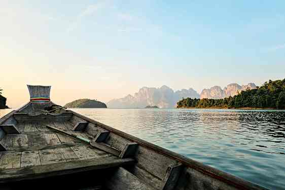 Billede af en træbåd, der sejler mod bjerge på en sø. (AI-genereret tekst)