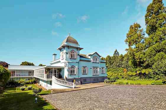 En lyseblå bygning med store vinduer og grønne omgivelser. (AI-genereret tekst)