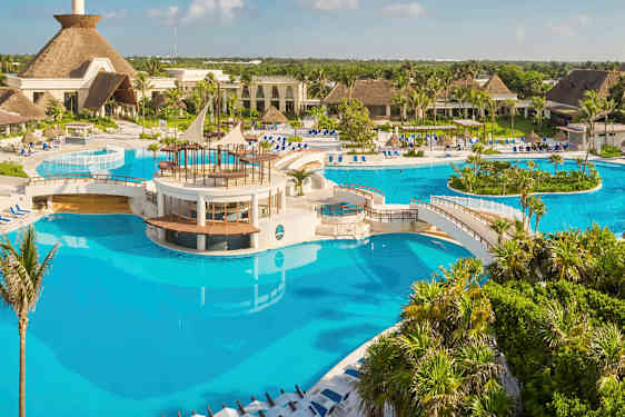 En stor pool med broer og et centralt område omgivet af tropiske planter og bygninger. (AI-genereret tekst)