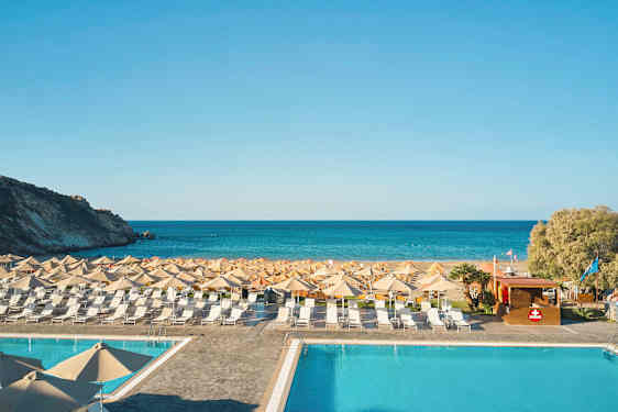 En pool foran en strand med liggestole og parasoller, og havet i baggrunden. (AI-genereret tekst)