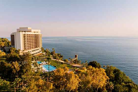 Hotelbygning med pool og grønne områder foran havet. (AI-genereret tekst)