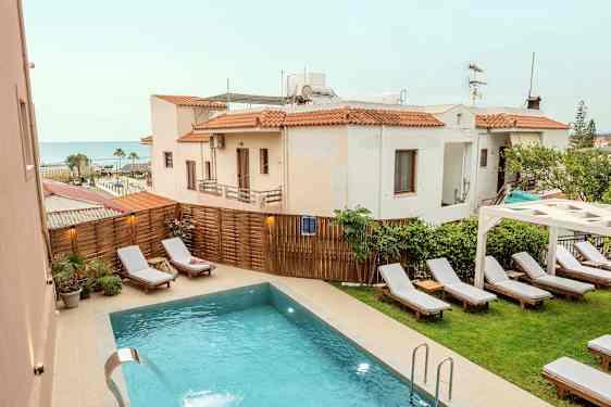 Udendørs pool med liggestole og omkringliggende bygninger i baggrunden. (AI-genereret tekst)