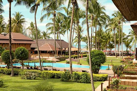 Resortområde med frodige haver, pool og palmer tæt på havet. (AI-genereret tekst)