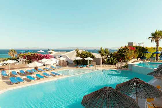 En udendørs pool omgivet af liggestole og parasoller med udsigt over havet og den omkringliggende vegetation. (AI-genereret tekst)