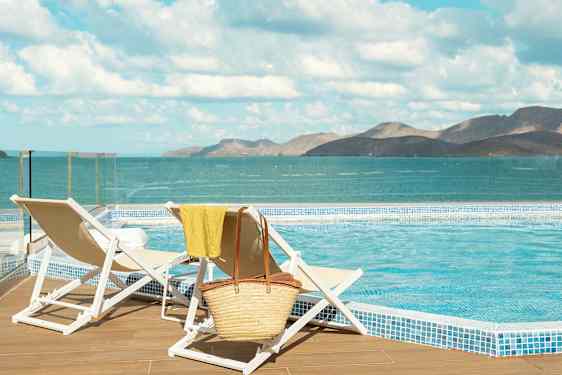To liggestole ved en pool med udsigt over havet og bjerge i baggrunden. (AI-genereret tekst)