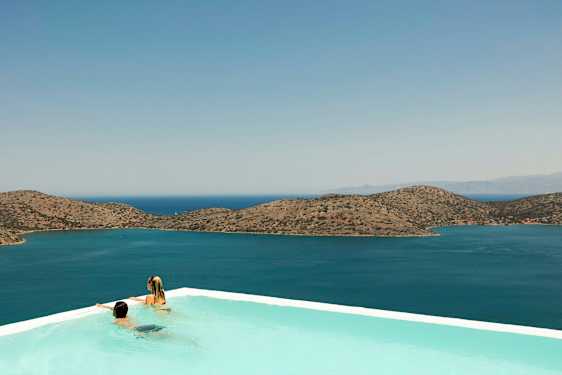 To personer i en infinitypool med udsigt over havet og bjerge i baggrunden. (AI-genereret tekst)