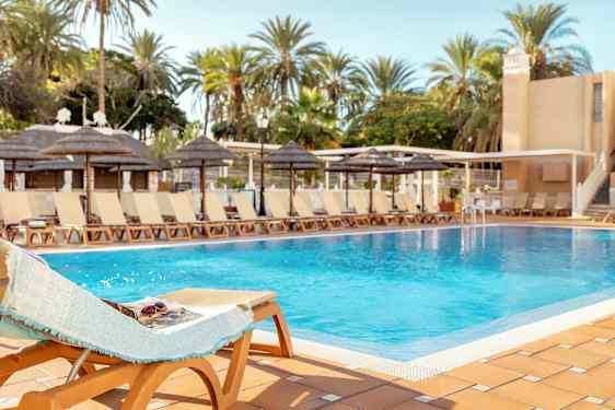 En pool omgivet af liggestole og palmer under en klar himmel. (AI-genereret tekst)