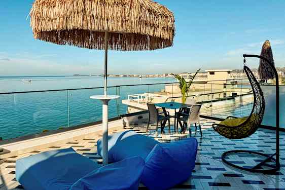 En tagterrasse med udsigt over havet, med siddepladser, en parasol og en hængestol. (AI-genereret tekst)