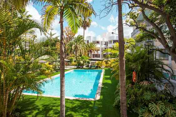 En udendørs pool omgivet af palmer og bygninger. (AI-genereret tekst)