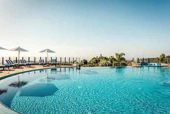 Udendørs pool med liggestole og parasoller omkring kanten samt udsigt over landskab med vegetation. (AI-genereret tekst)