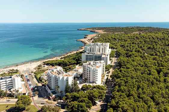 Luftfoto af en kystlinje med hotelbygninger foran en skov og tæt på en strand. (AI-genereret tekst)