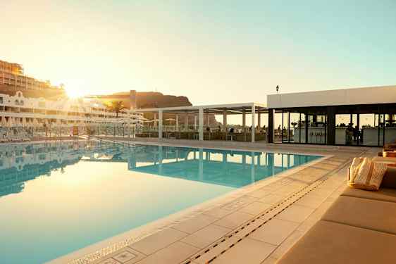 Udendørs swimmingpool ved et hotel med liggestole og en bygning i baggrunden. (AI-genereret tekst)