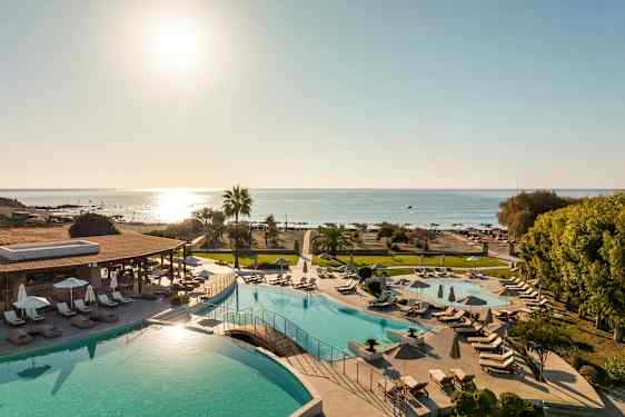 Udsigt over et poolområde med solsenge og parasoller samt stranden og havet i baggrunden. (AI-genereret tekst)