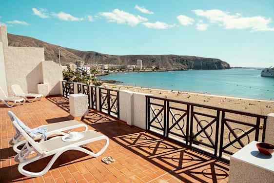 Terrasse med liggestole og udsigt over en sandstrand med havet i horisonten. (AI-genereret tekst)