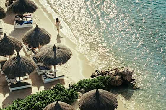 En sandstrand med parasoller og liggestole ved siden af et klart hav. (AI-genereret tekst)