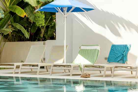 Liggestole og parasol ved poolen, med bananplanter i baggrunden. (AI-genereret tekst)