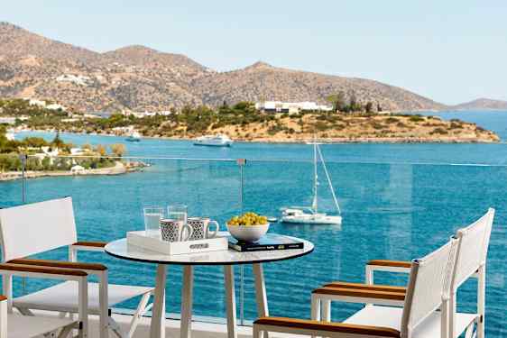 En terrasse med bord og stole med udsigt over havet og en ø. (AI-genereret tekst)