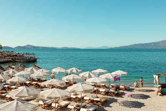 Strand med liggestole og parasoller ved klart blåt vand. (AI-genereret tekst)