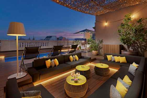 En terrasse med moderne møbler, en pool og belysning ved solnedgang. (AI-genereret tekst)