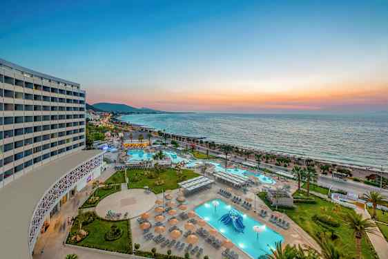 Billede af et feriested med pools og liggestole ved havet under solnedgangen. (AI-genereret tekst)