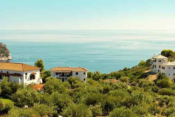 Et landskab med hvide huse og tegltage omgivet af grøn vegetation og med udsigt over et roligt blåt hav. (AI-genereret tekst)