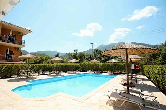 Udendørs pool omgivet af liggestole og parasoller, med grønt og bjerge i baggrunden. (AI-genereret tekst)