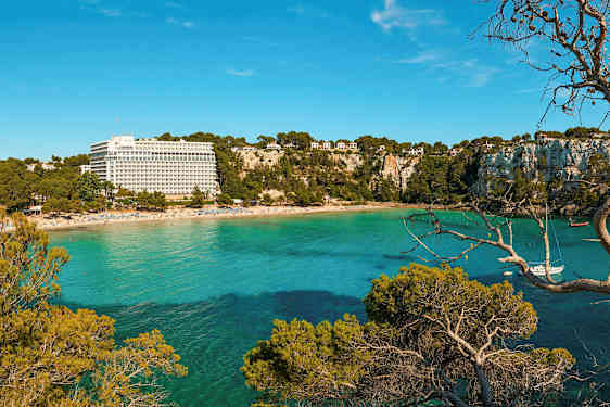 En strand med en resortbygning og frodige klipper ved et turkisblåt hav. (AI-genereret tekst)