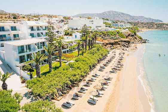 Strand med liggestole og parasoller ved en hotelbygning omgivet af grønt. (AI-genereret tekst)