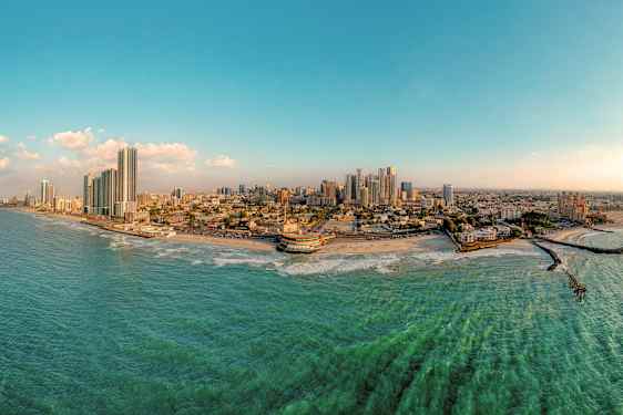 Panoramabillede af en kystby med højhuse, strand og hav. (AI-genereret tekst)