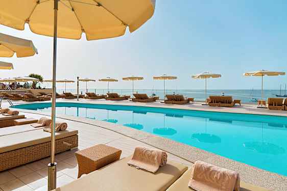 Liggestole med parasoller omkring en pool, og udsigt over havet. (AI-genereret tekst)