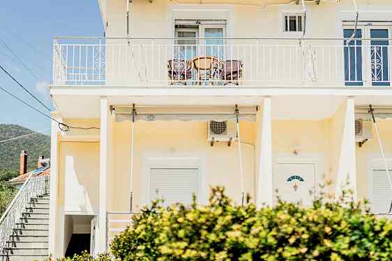 En gul bygning med en altan øverst og buske i forgrunden. (AI-genereret tekst)