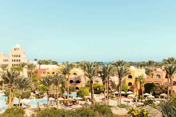 Et feriested med palmer og farverige bygninger, havet kan ses i baggrunden. (AI-genereret tekst)